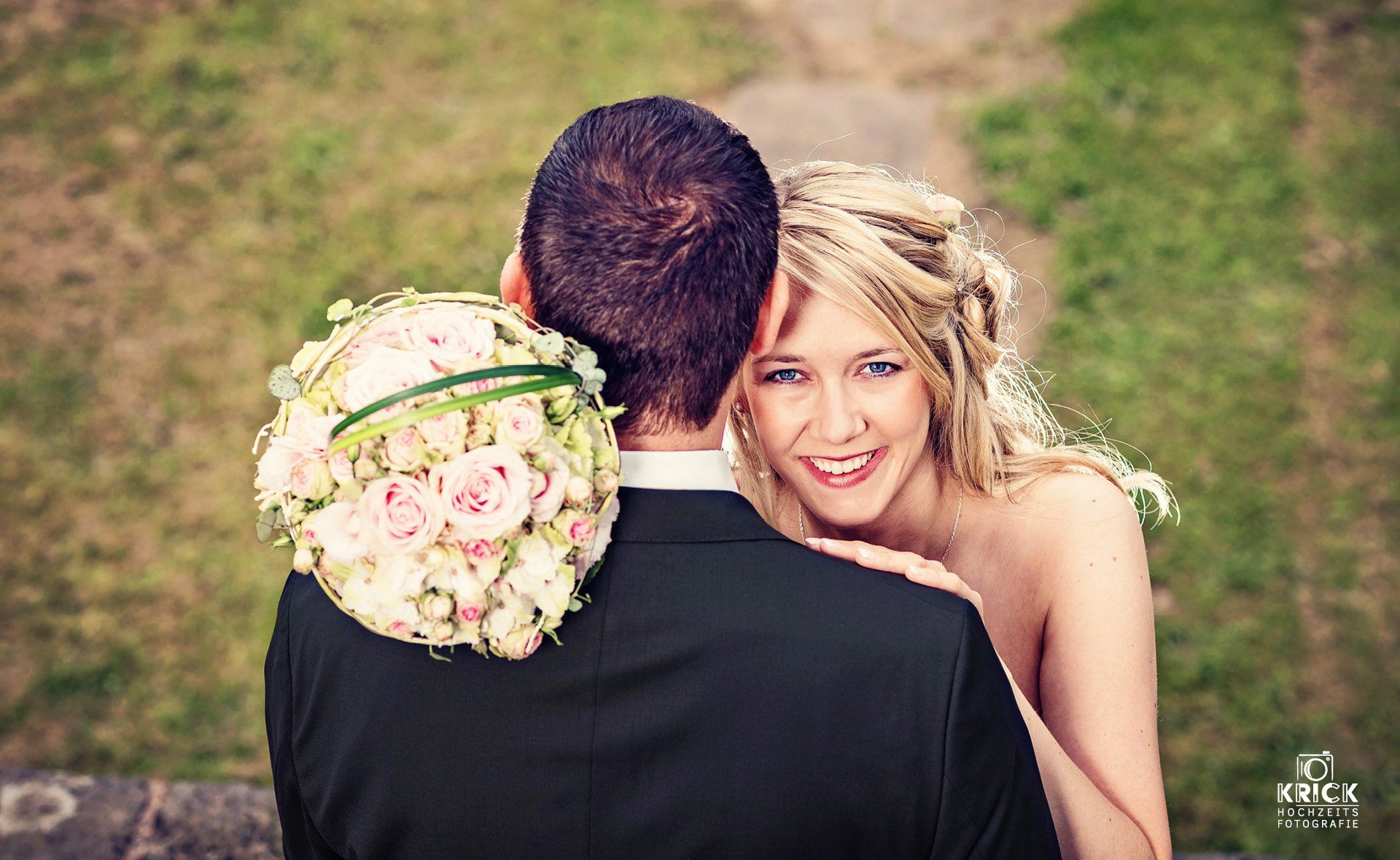 Eine Braut und ein Bräutigam posieren für ein Foto und die Braut trägt einen Blumenstrauß auf ihrer Schulter.