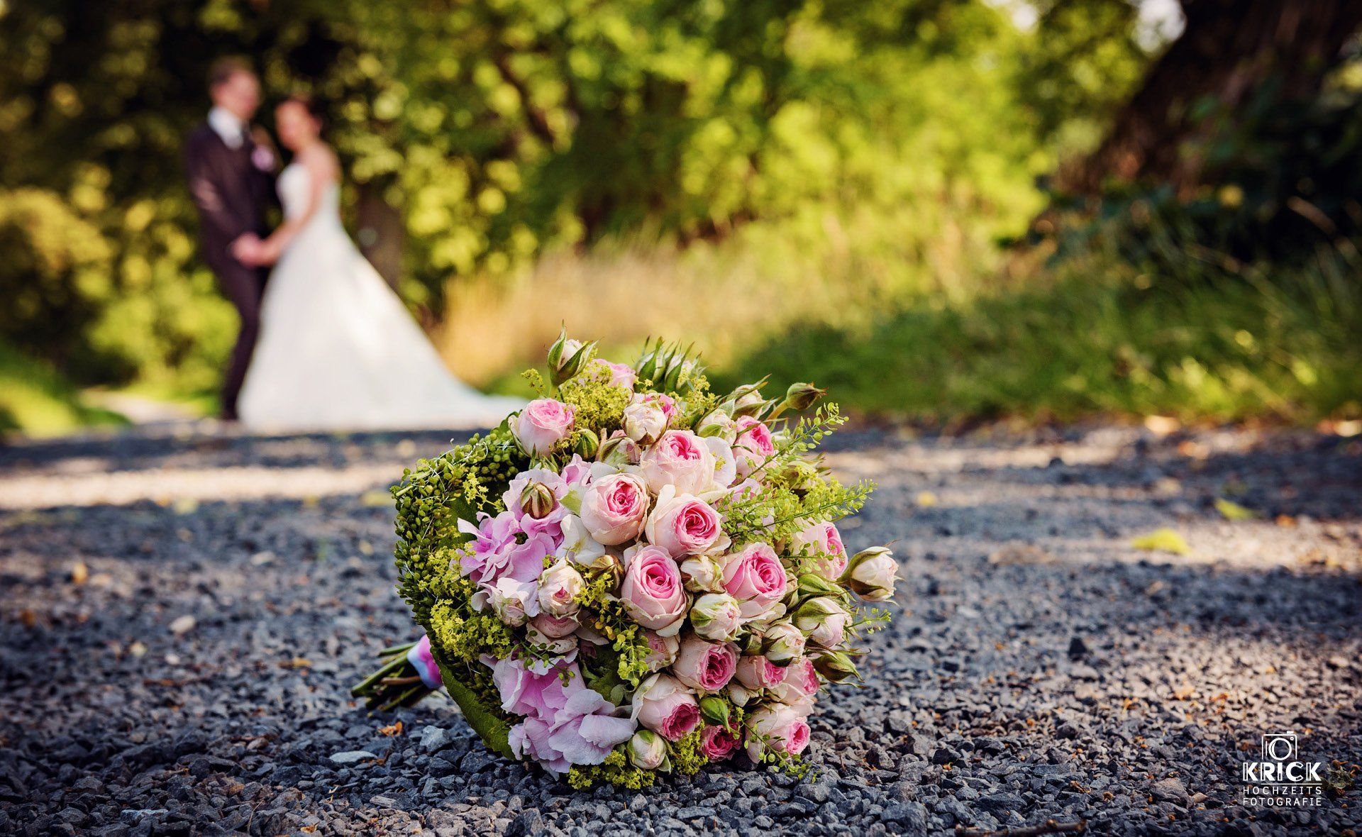 Ein Strauß rosa Rosen liegt neben Braut und Bräutigam auf dem Boden.