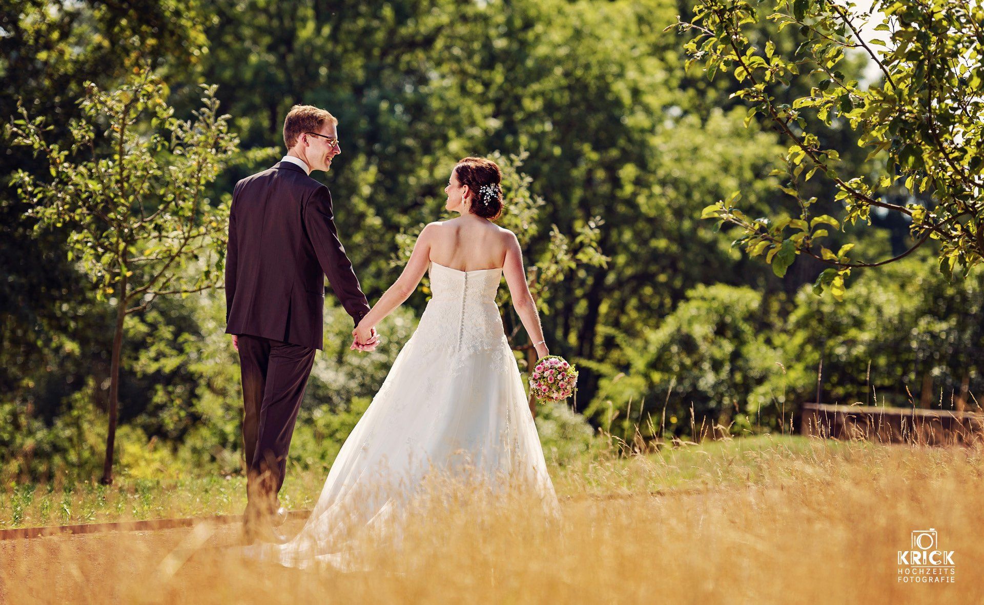 Eine Braut und ein Bräutigam gehen Hand in Hand durch ein Feld.