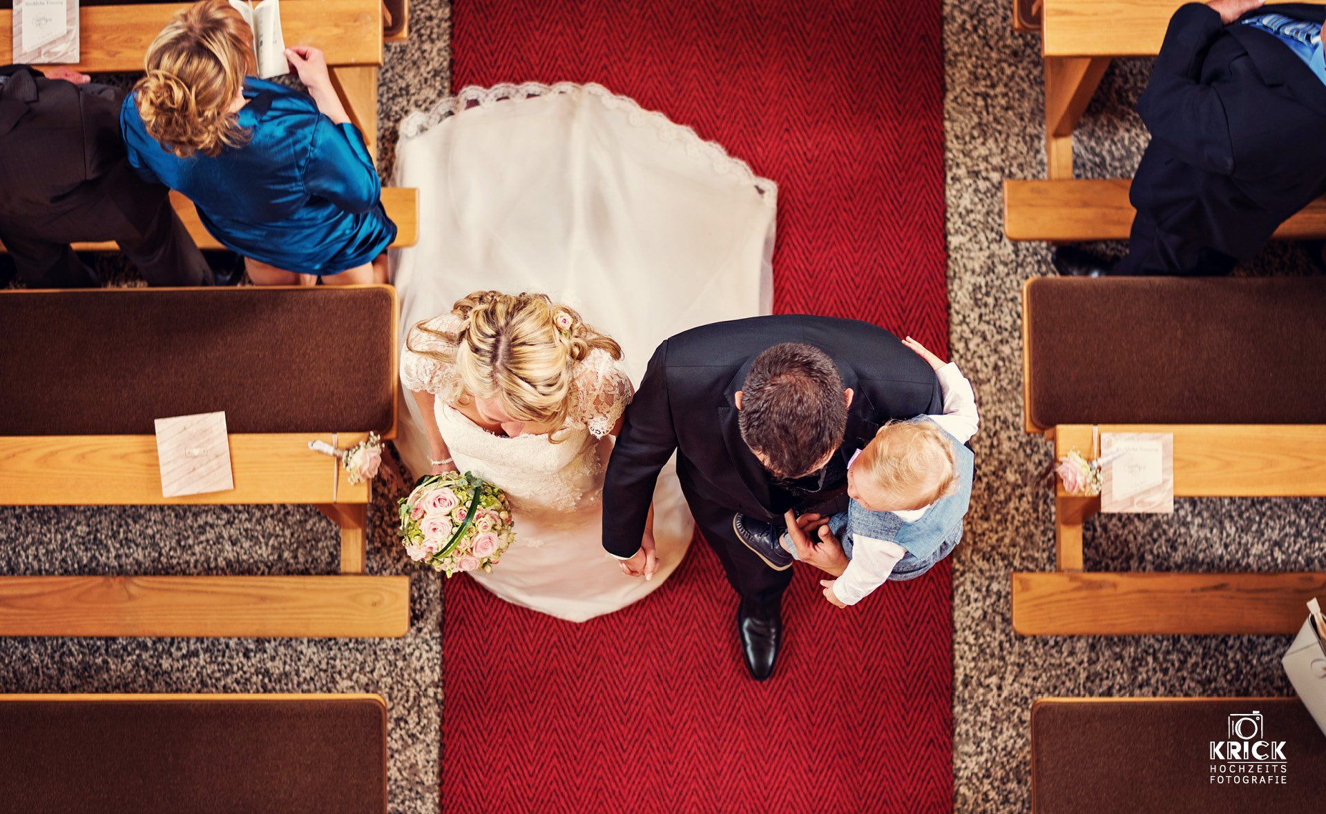Eine Braut und ein Bräutigam sitzen auf einem roten Teppich in einer Kirche.