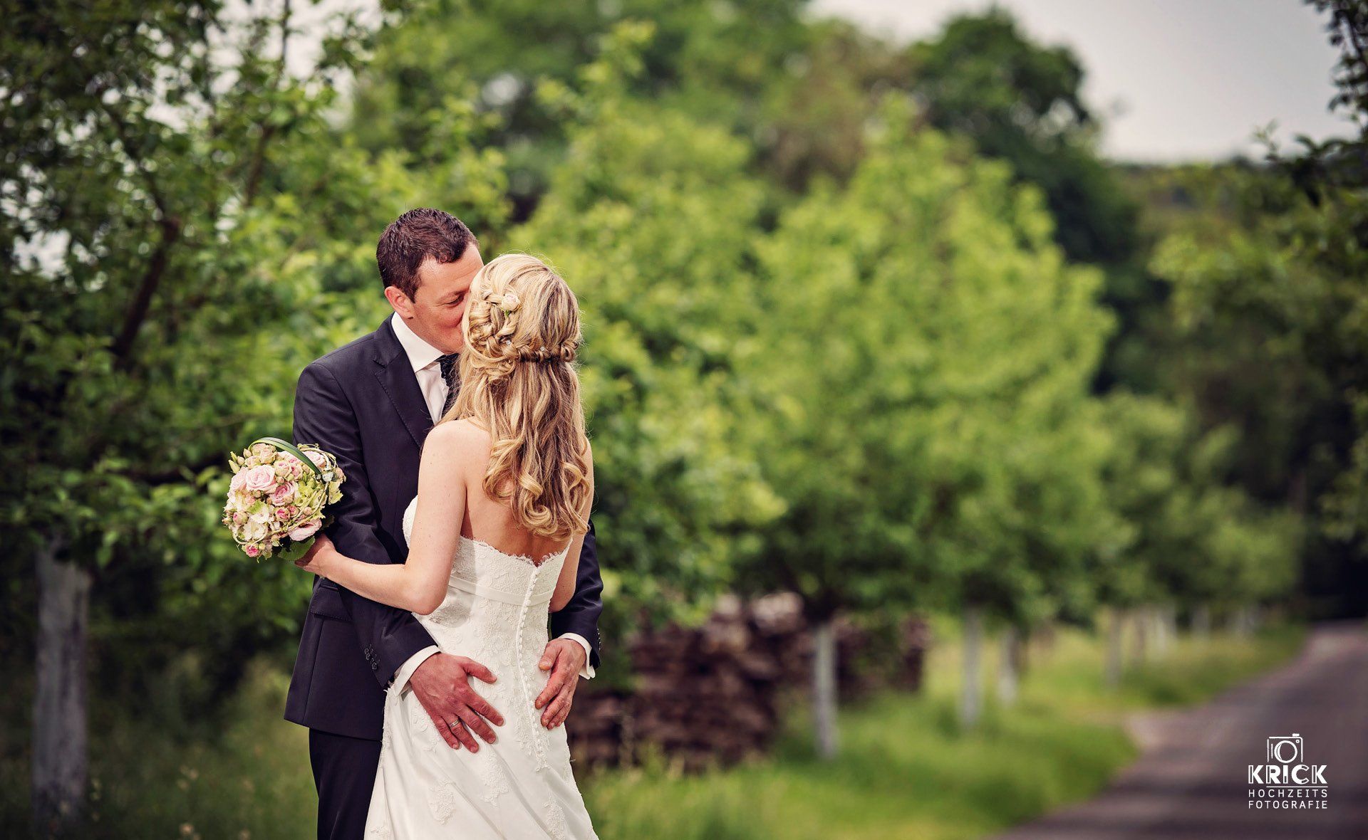 Eine Braut und ein Bräutigam küssen sich auf einem Feld.