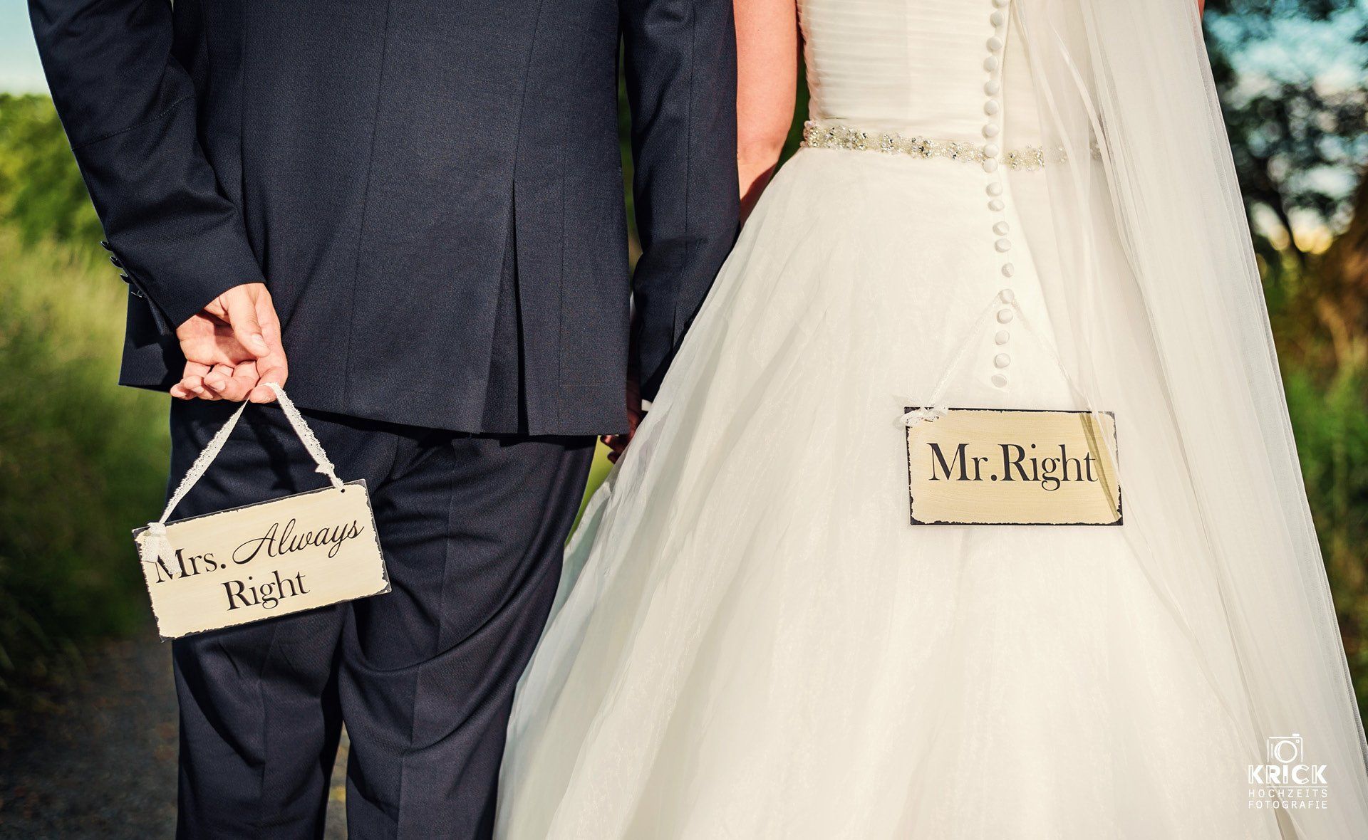 Eine Braut und ein Bräutigam halten Händchen mit Schildern, auf denen „Mr. Right“ und „Mrs. Always Right“ steht