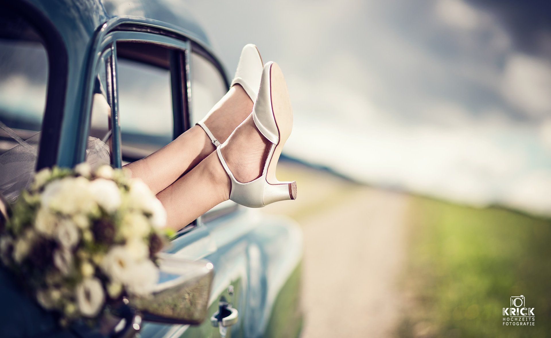 Eine Braut sitzt in einem Auto und hat ihre Füße aus dem Fenster gestreckt.