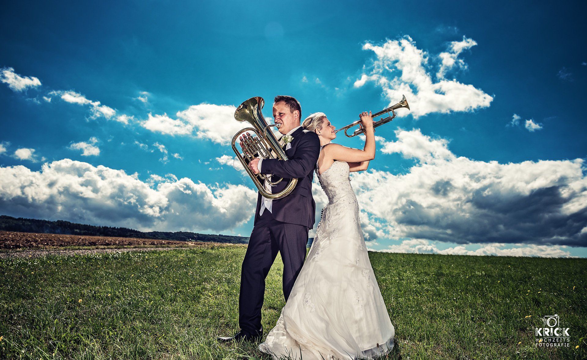 Eine Braut und ein Bräutigam stehen mit einer Trompete in der Hand auf einem Feld.