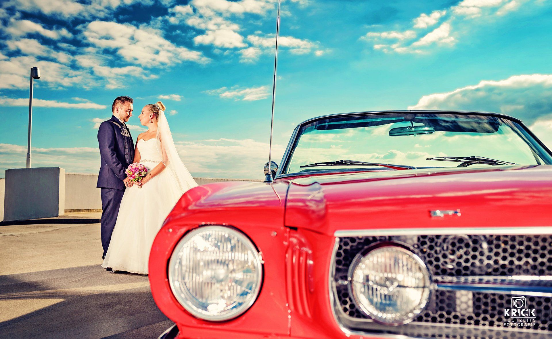 Eine Braut und ein Bräutigam stehen neben einem roten Cabrio.