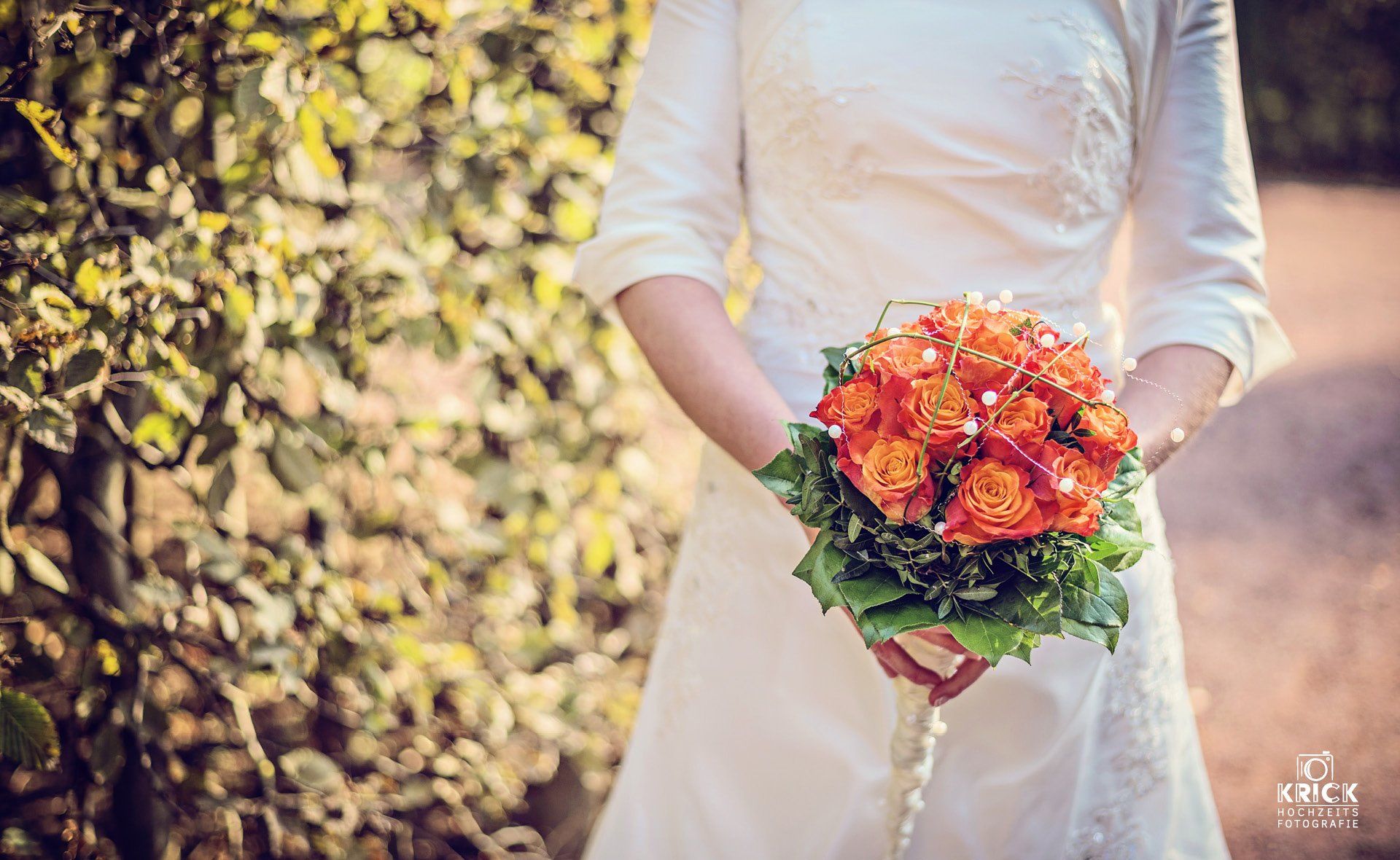 Eine Braut in einem weißen Kleid hält einen Strauß orangefarbener Blumen.