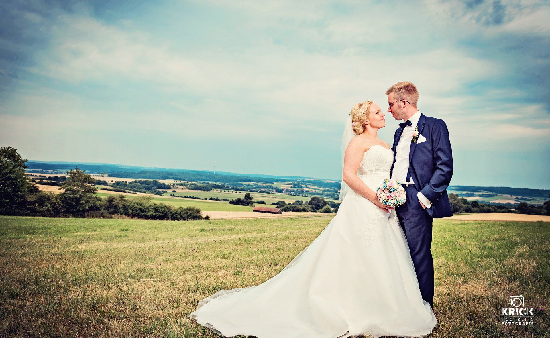 Eine Braut und ein Bräutigam küssen sich auf einem Feld.