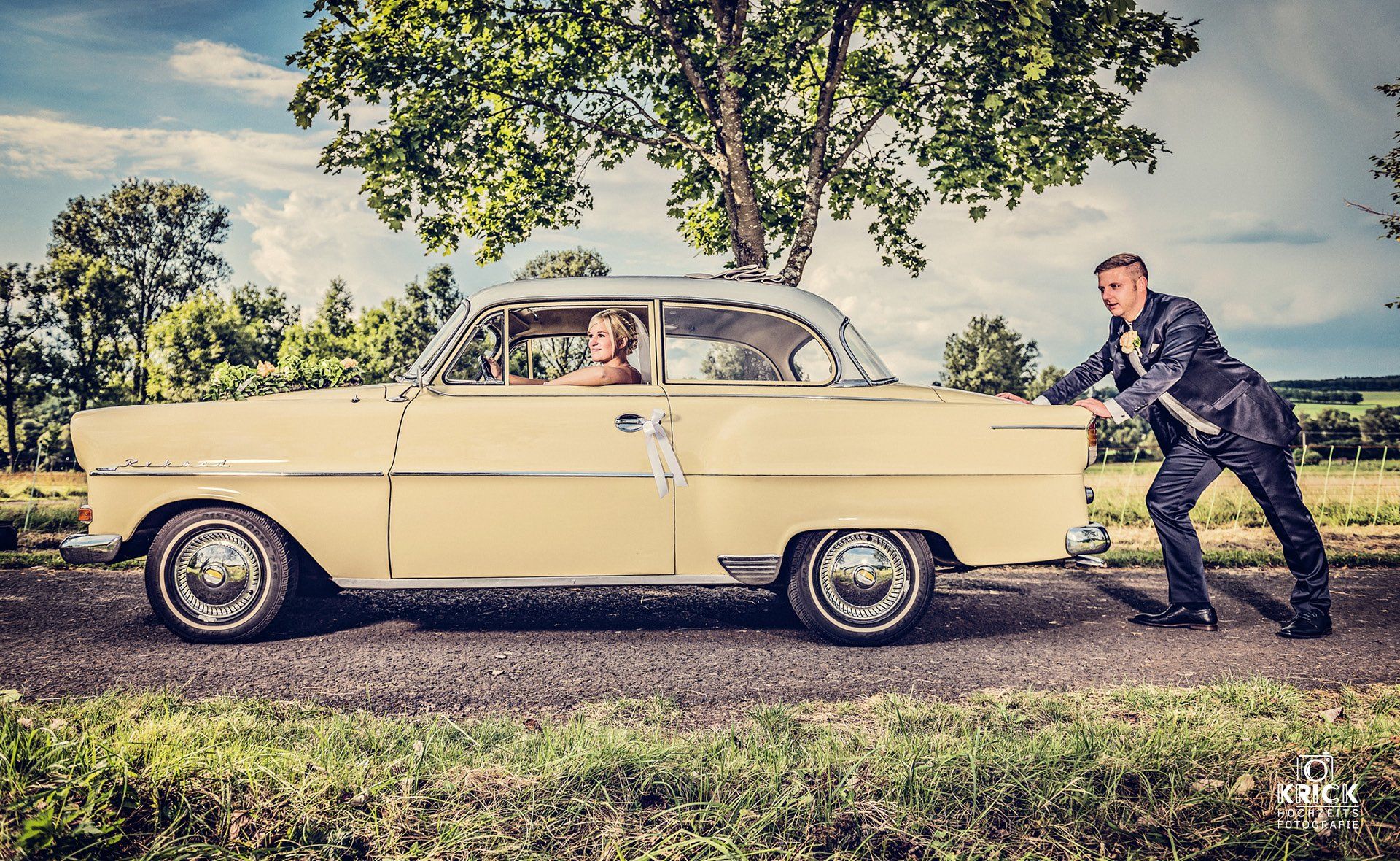 Eine Braut und ein Bräutigam schieben ein gelbes Auto eine Straße entlang.