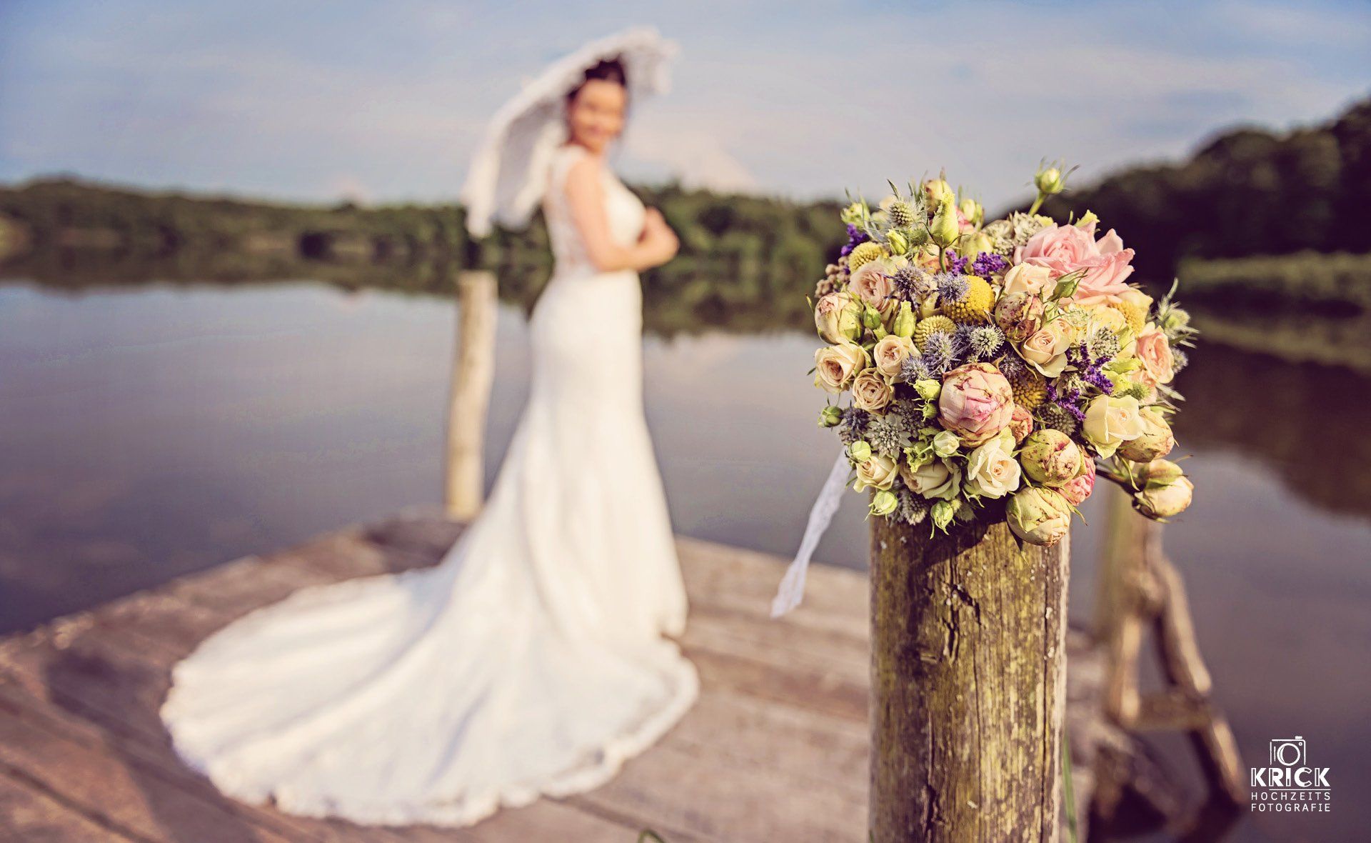 Eine Braut im Hochzeitskleid steht auf einem Steg neben einer Vase mit Blumen.
