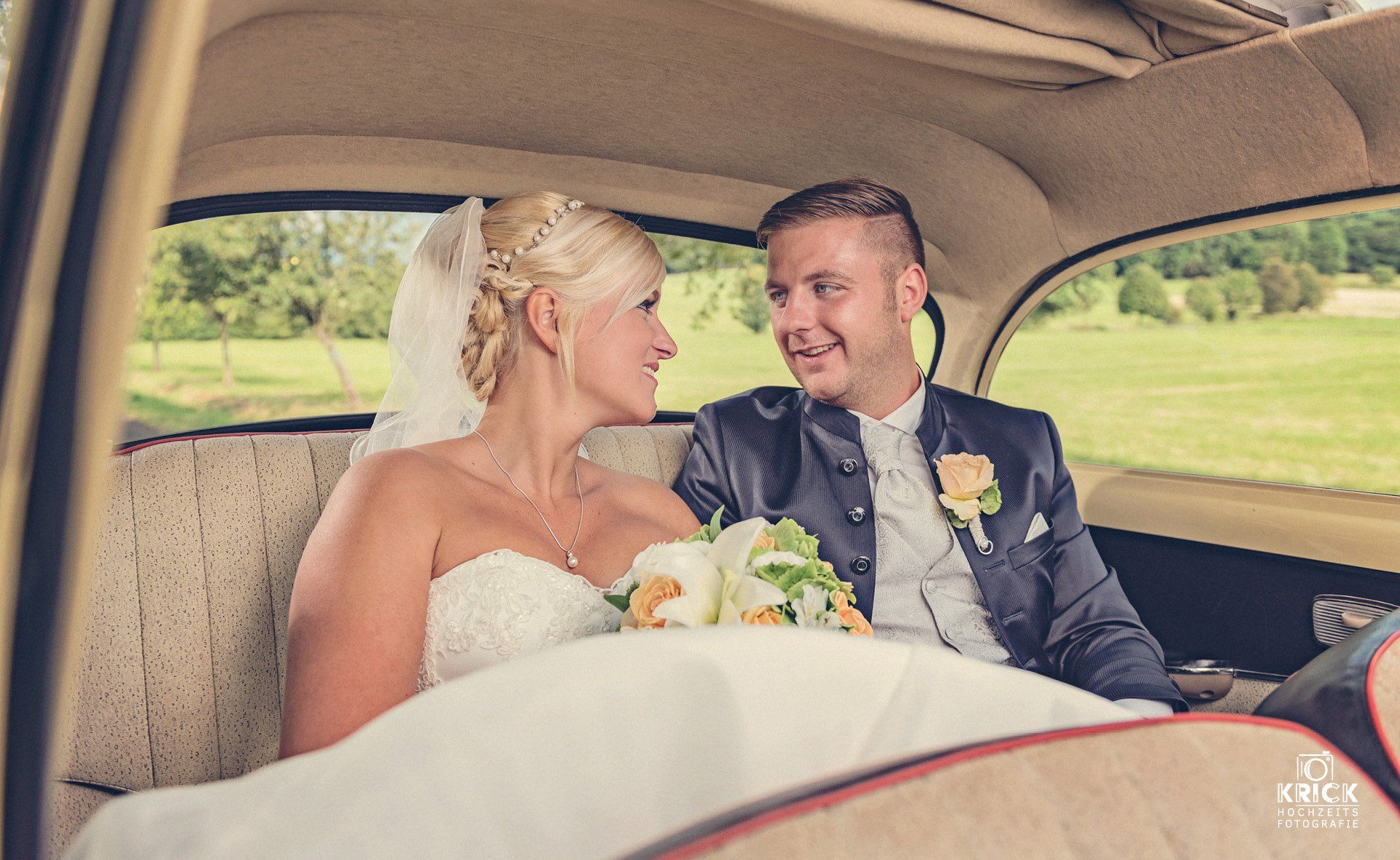 Eine Braut und ein Bräutigam sitzen auf dem Rücksitz eines Autos und schauen einander an.