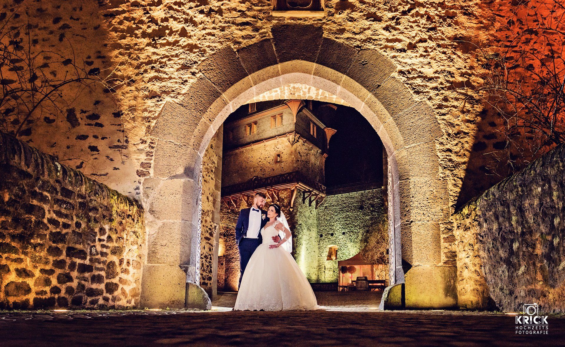 Eine Braut und ein Bräutigam posieren für ein Foto vor einem steinernen Torbogen.