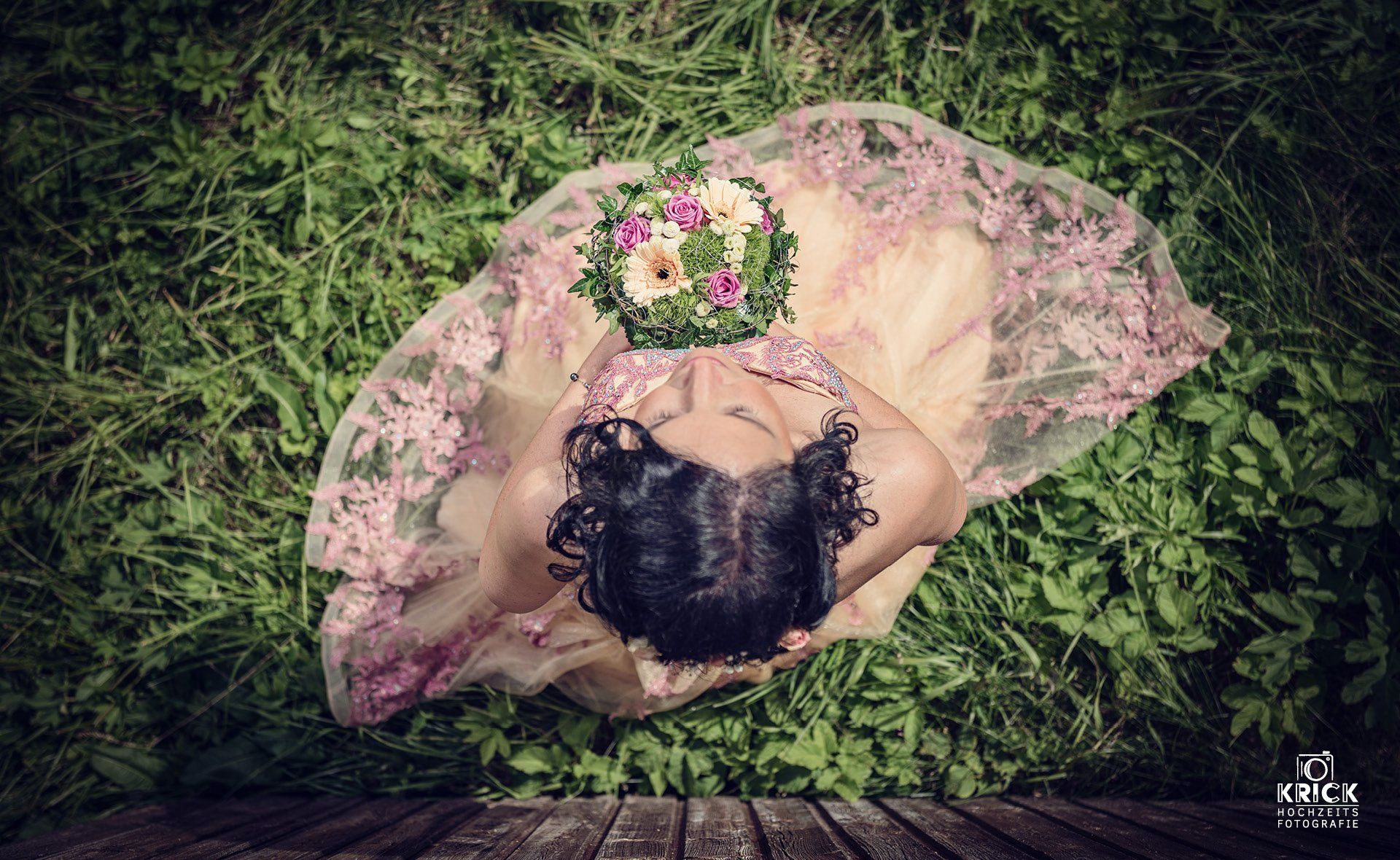 Eine Frau in einem rosa Kleid liegt im Gras und hält einen Blumenstrauß.