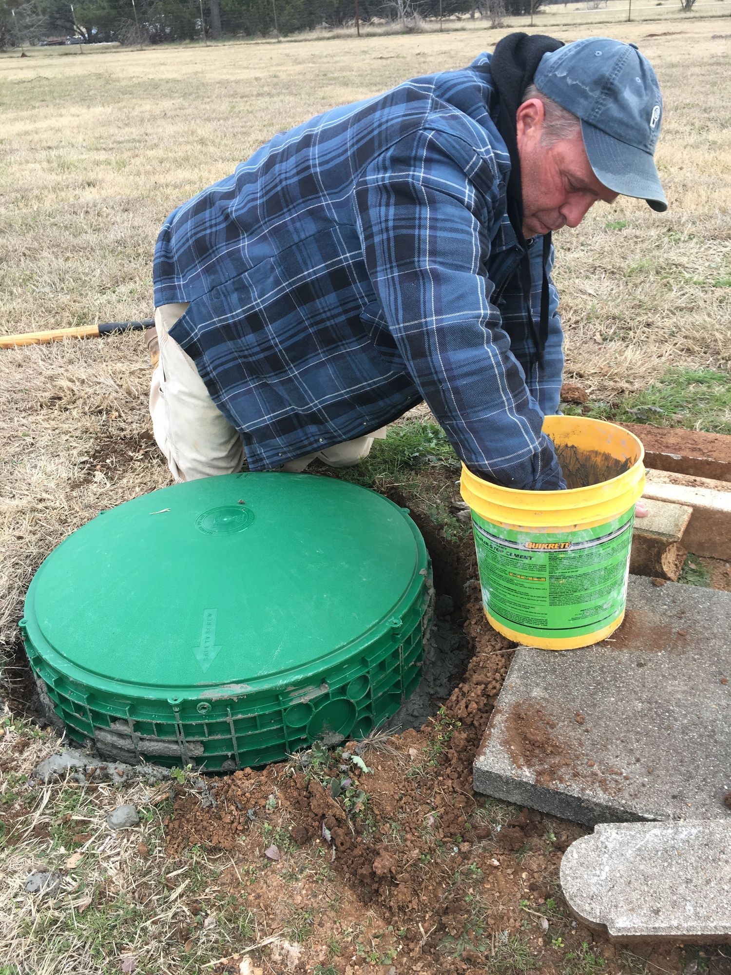 A man is kneeling down next to a bucket of dirt.