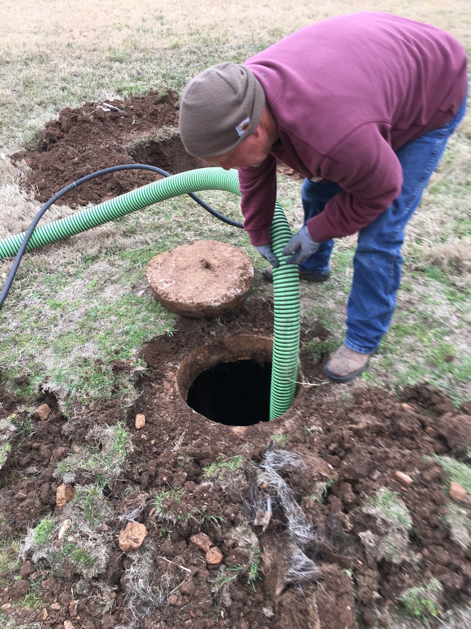 A man is pumping water into a septic tank with a green hose.