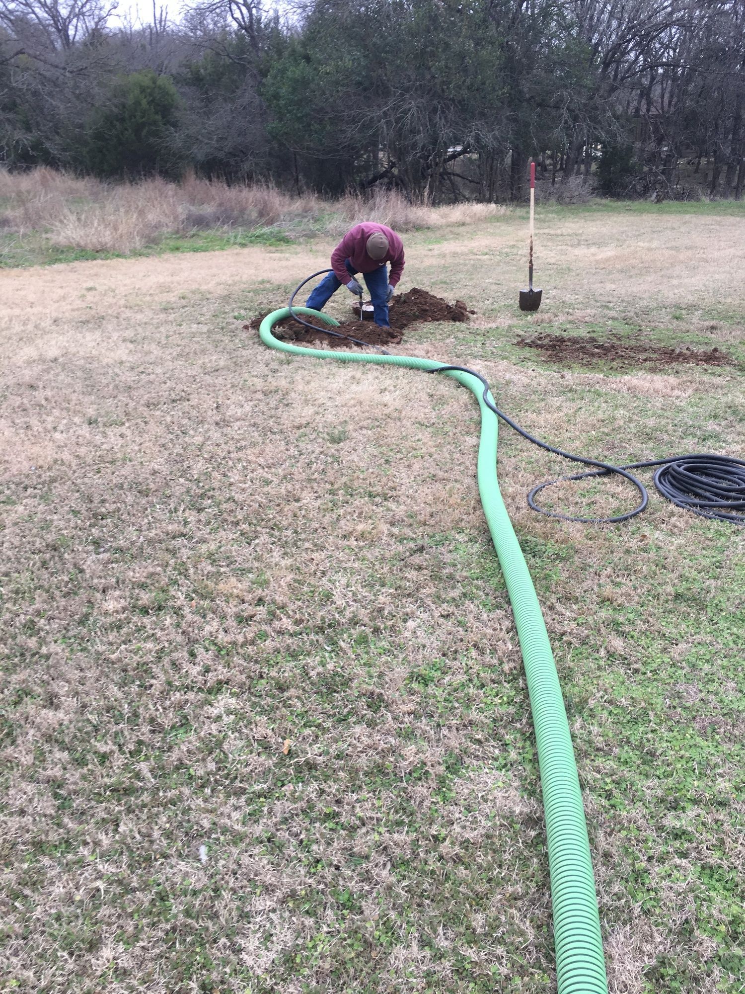 A man is digging a hole in the ground with a green hose.