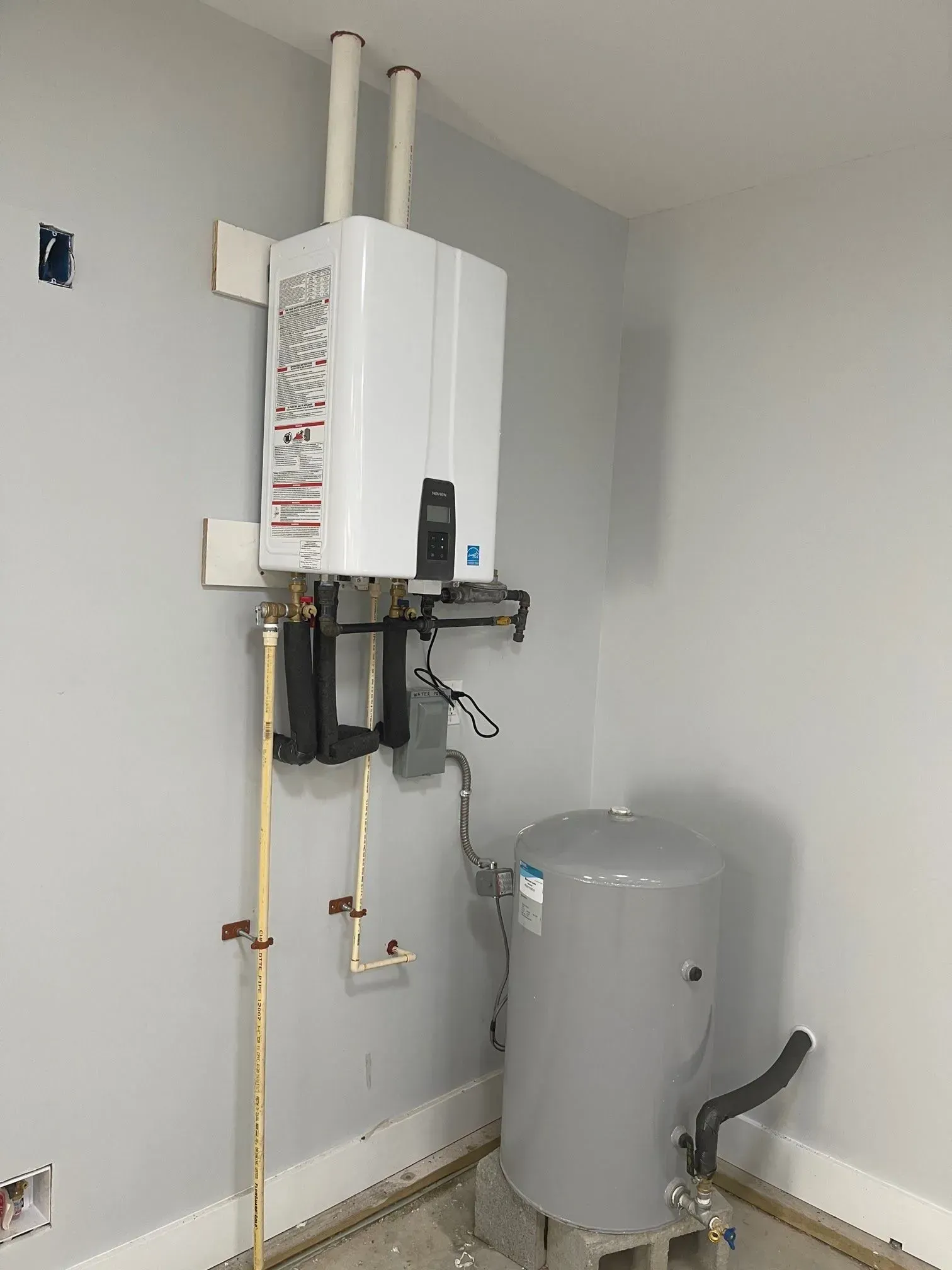 White tankless water heater and a grey water tank in a room with light gray walls.