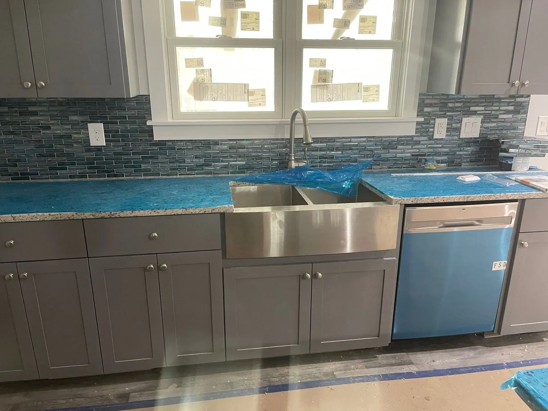 Gray kitchen cabinets with a stainless steel sink and blue tile backsplash.