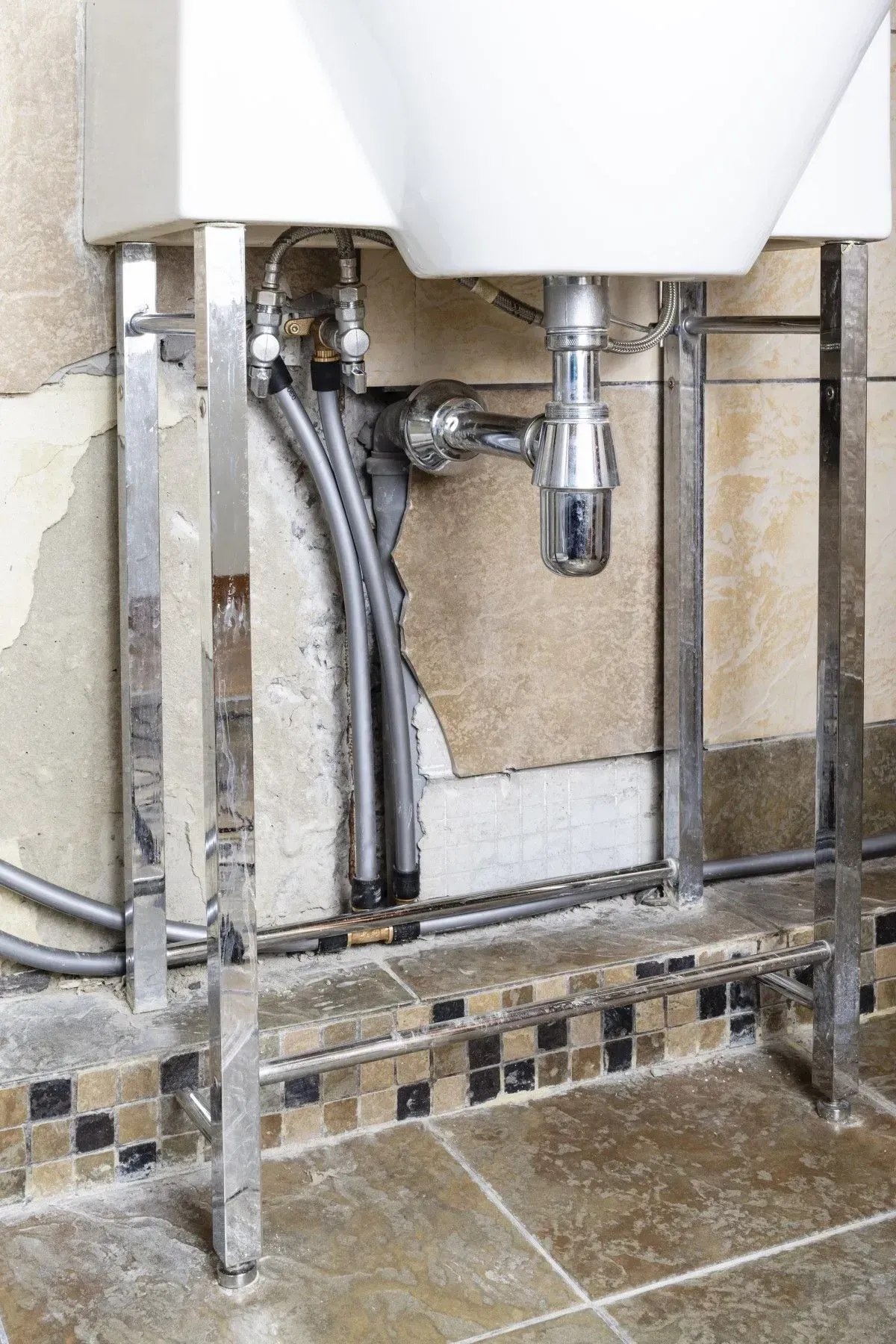 Bathroom sink with chrome frame and exposed pipes against peeling wall.