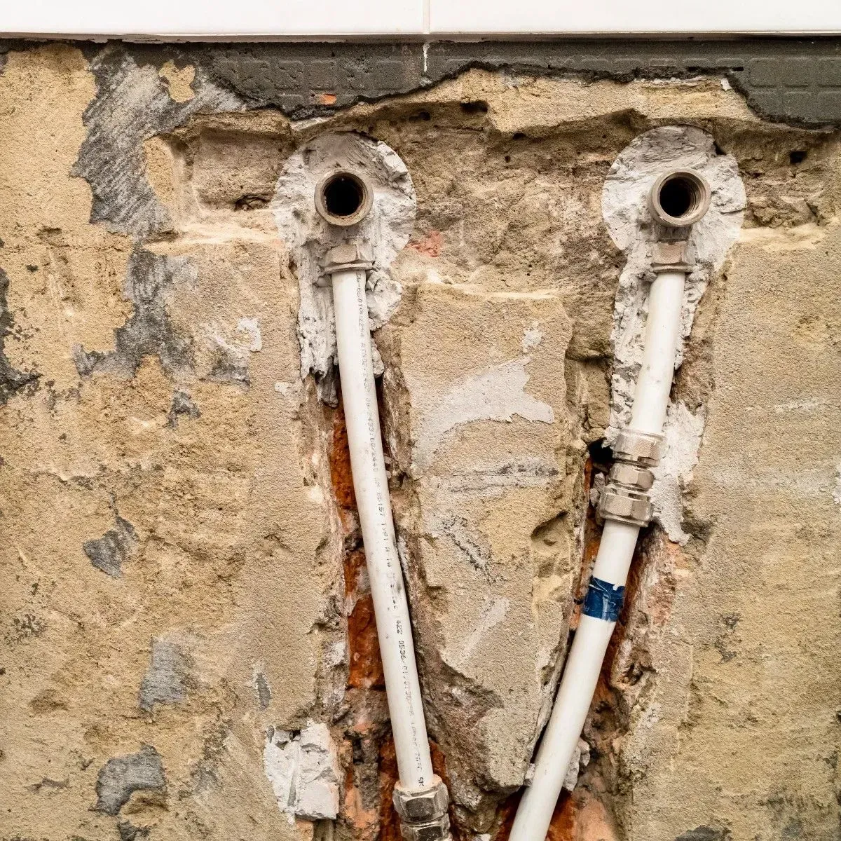 Two white pipes emerging from a wall with exposed brick and mortar.