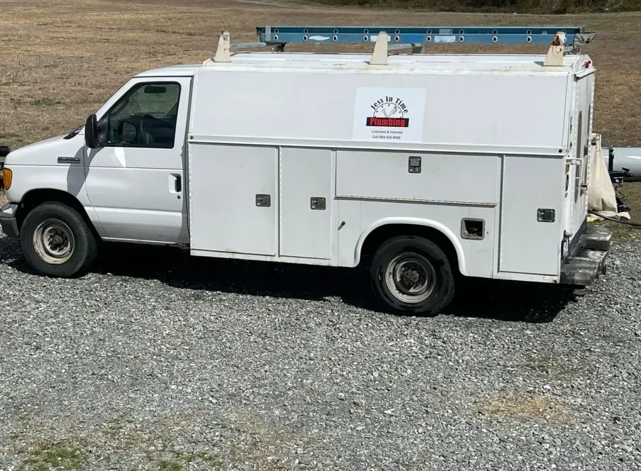 White work van with ladder on top, parked on gravel.