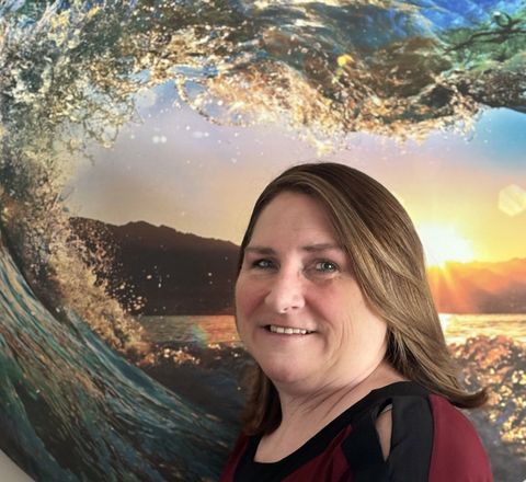 Tina Barnes is smiling in front of a painting of a wave
