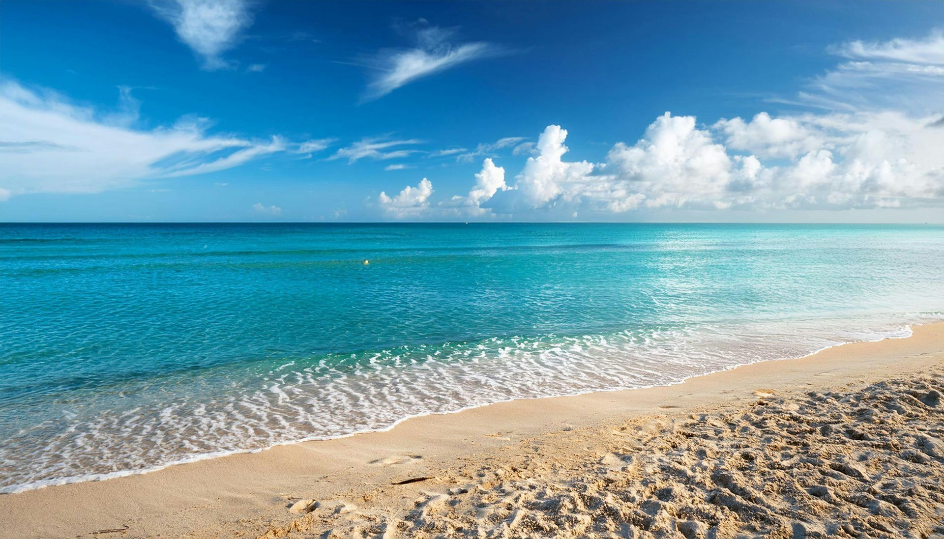 Sandy beach with turquoise water under a blue sky dotted with white clouds.
