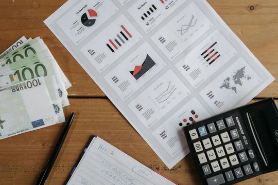 A calculator is sitting on a wooden table next to a pile of money.