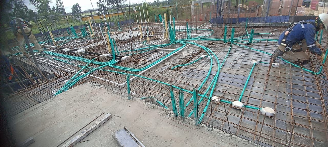 Sitio de construcción con tuberías verdes colocadas sobre una estructura de metal, un trabajador está arrodillado y trabaja en la estructura.