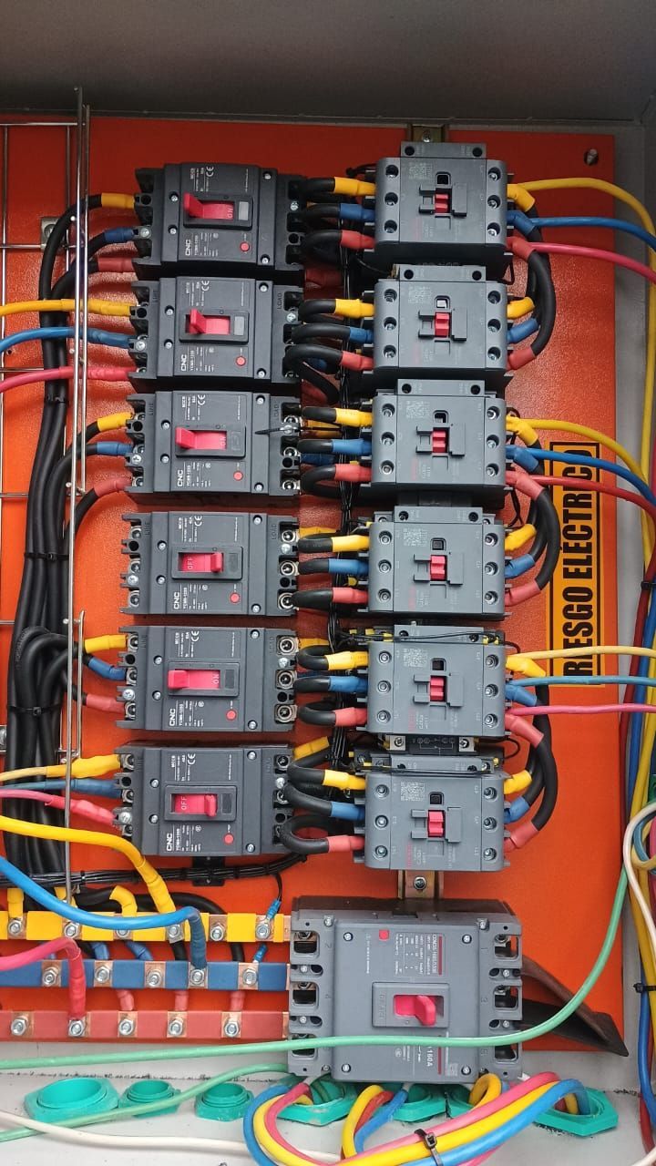 Panel eléctrico con disyuntores y cableado, mayoritariamente de color naranja y gris.
