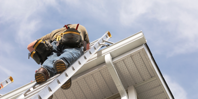 A man is sitting on a ladder on the roof of a house.