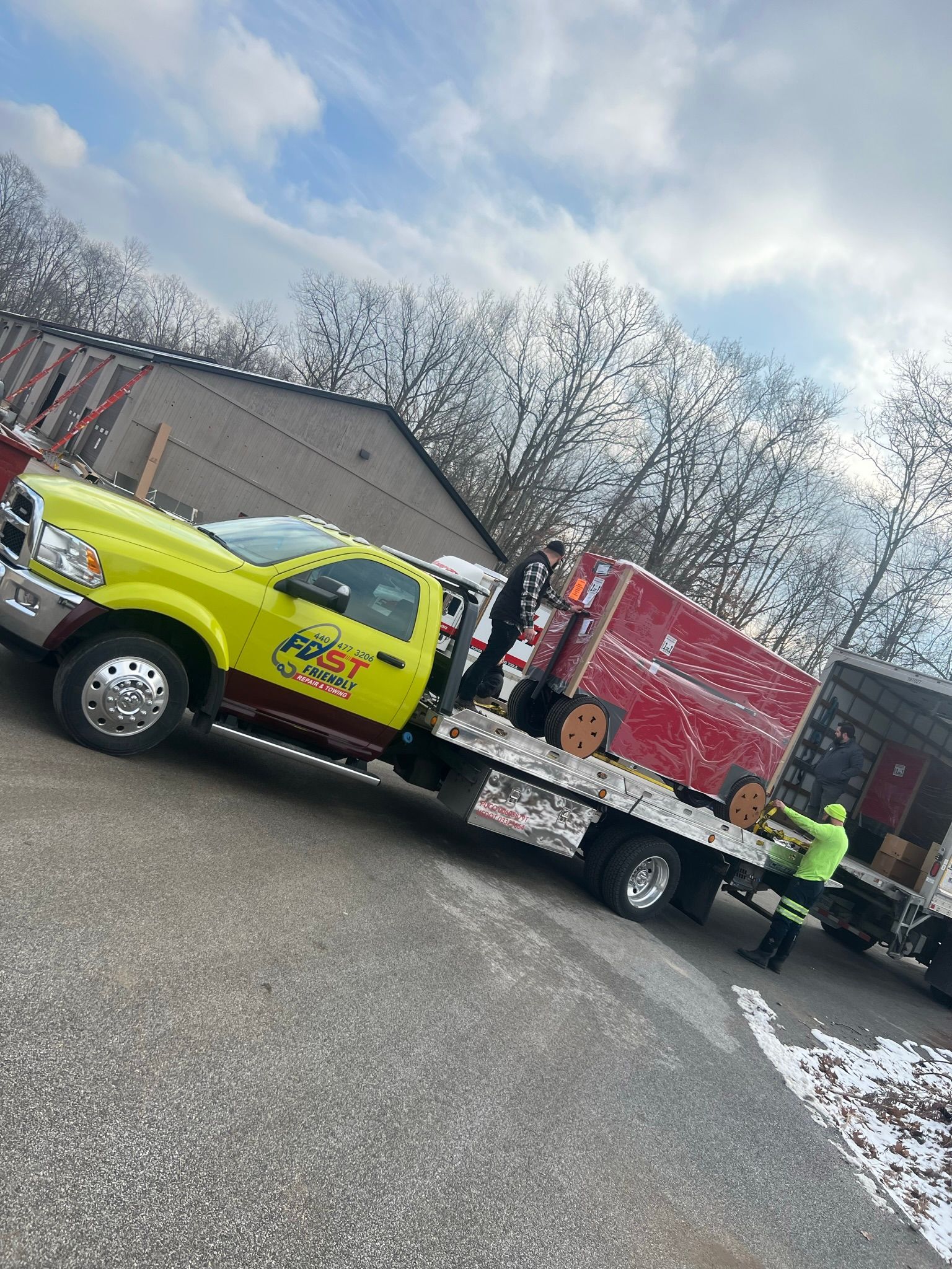 A yellow flatbed tow truck is towing a red truck.