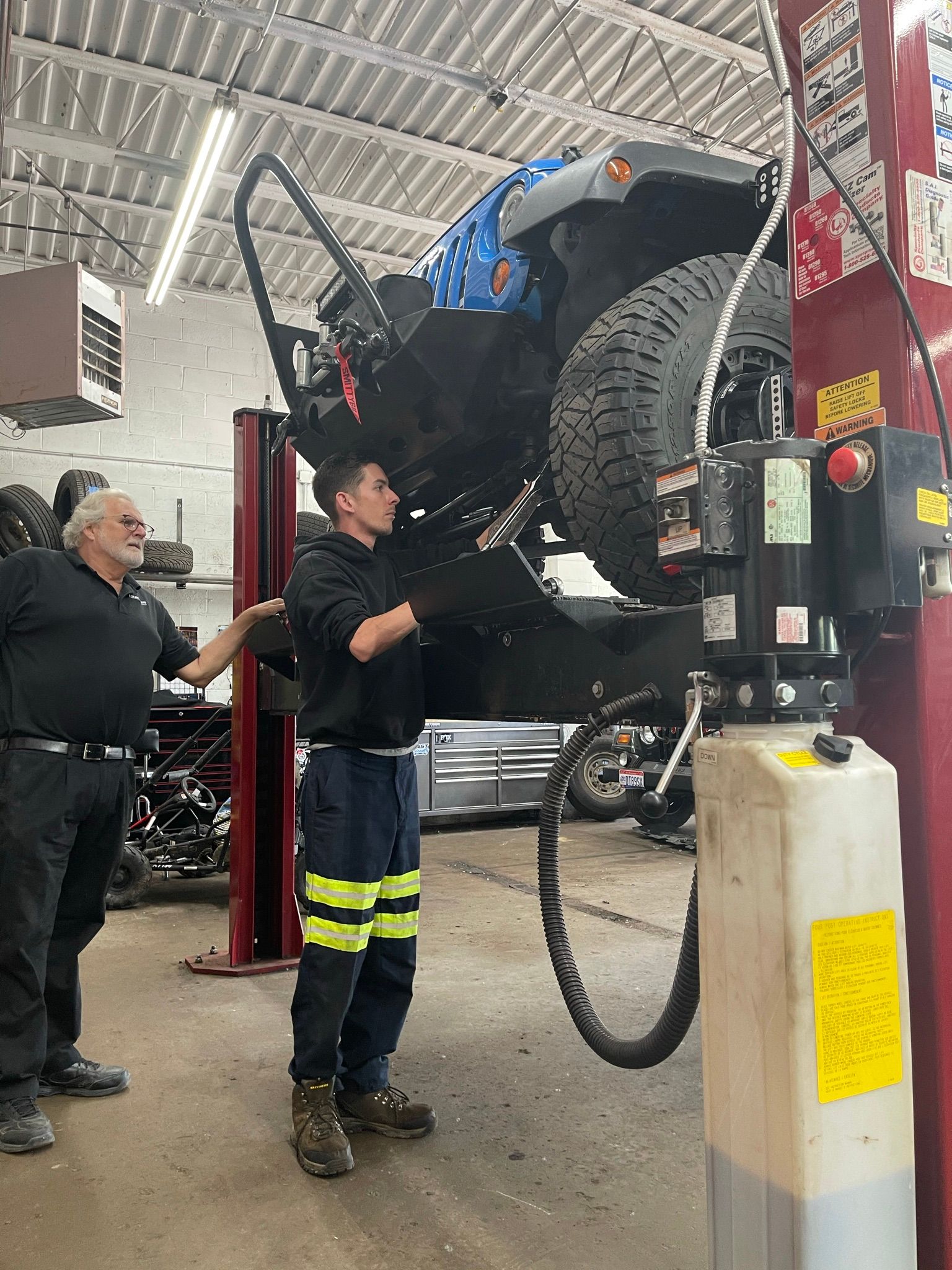 A man is working on a jeep on a lift in a garage.