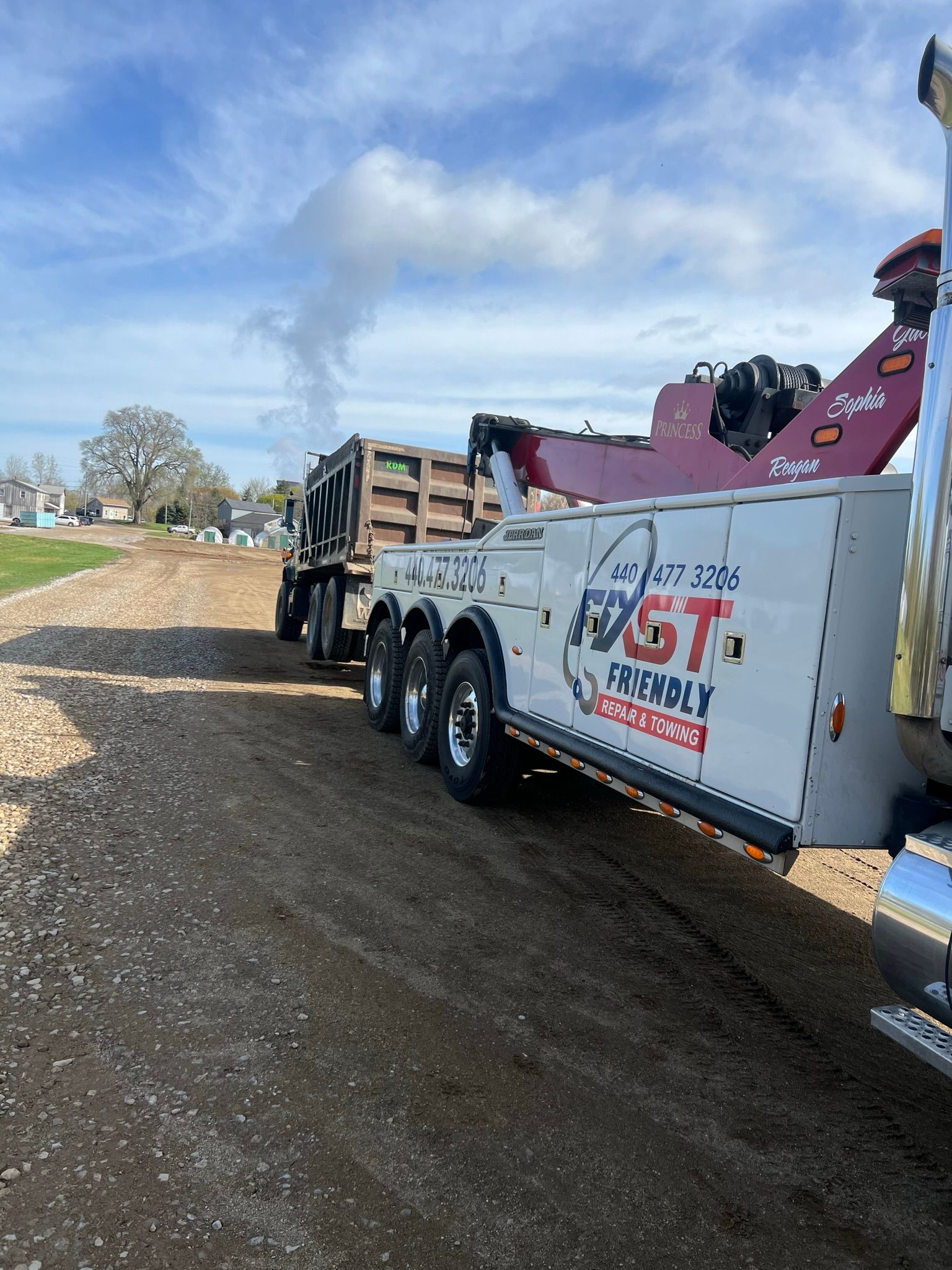 A tow truck is towing a dump truck down a dirt road.
