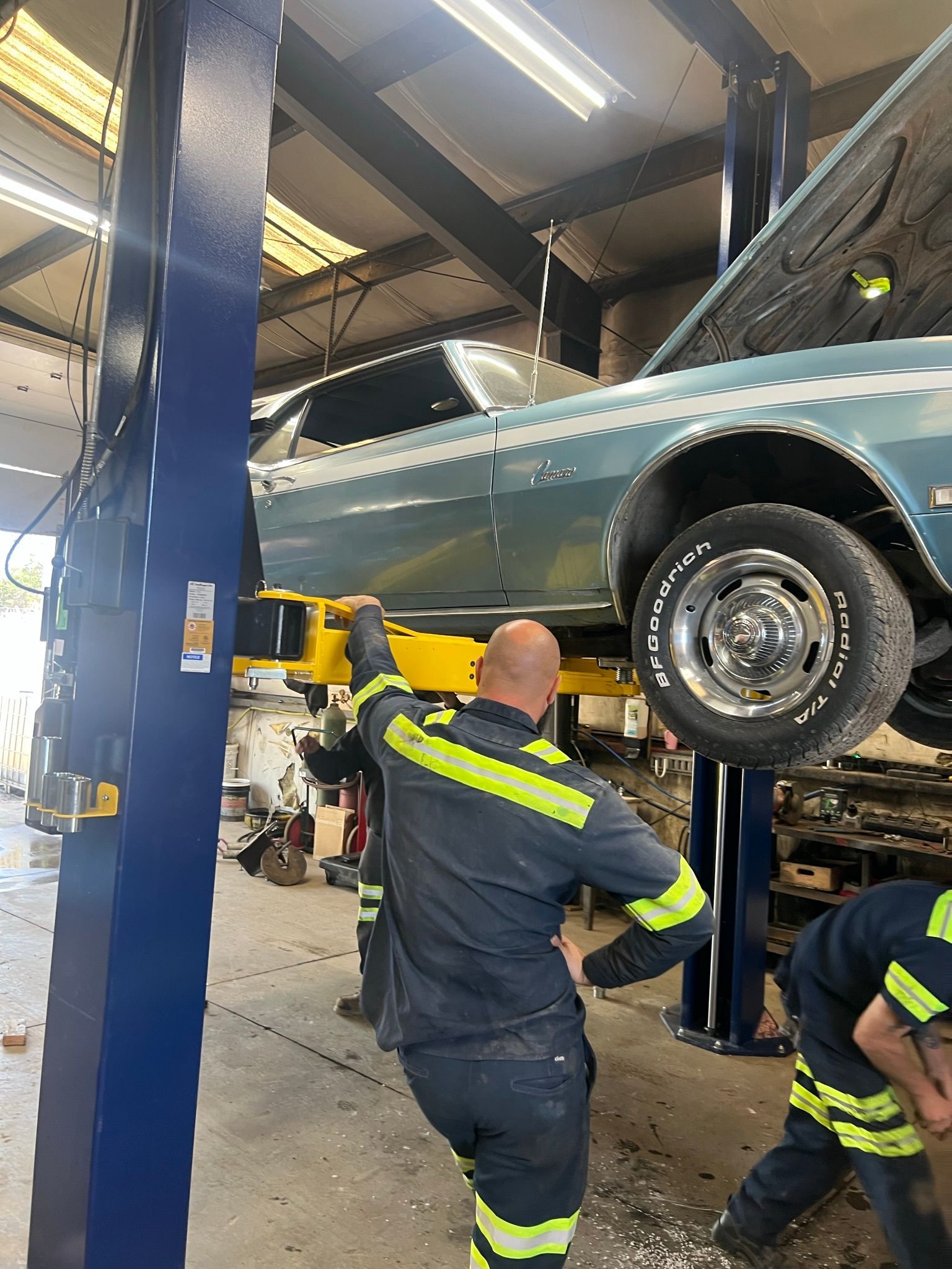 A man is working on a classic car on a lift in a garage.