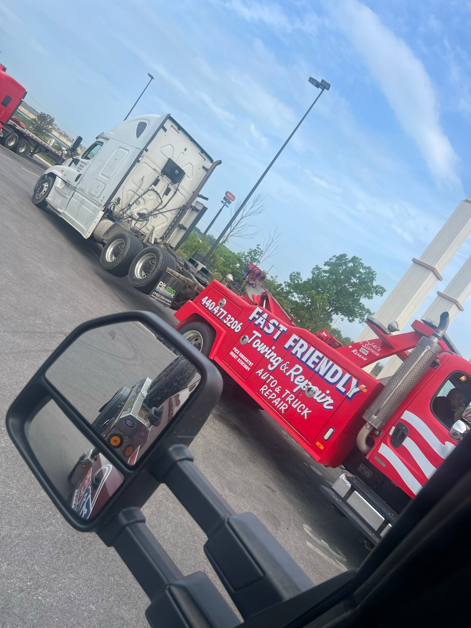 A red tow truck is parked next to a white semi truck.