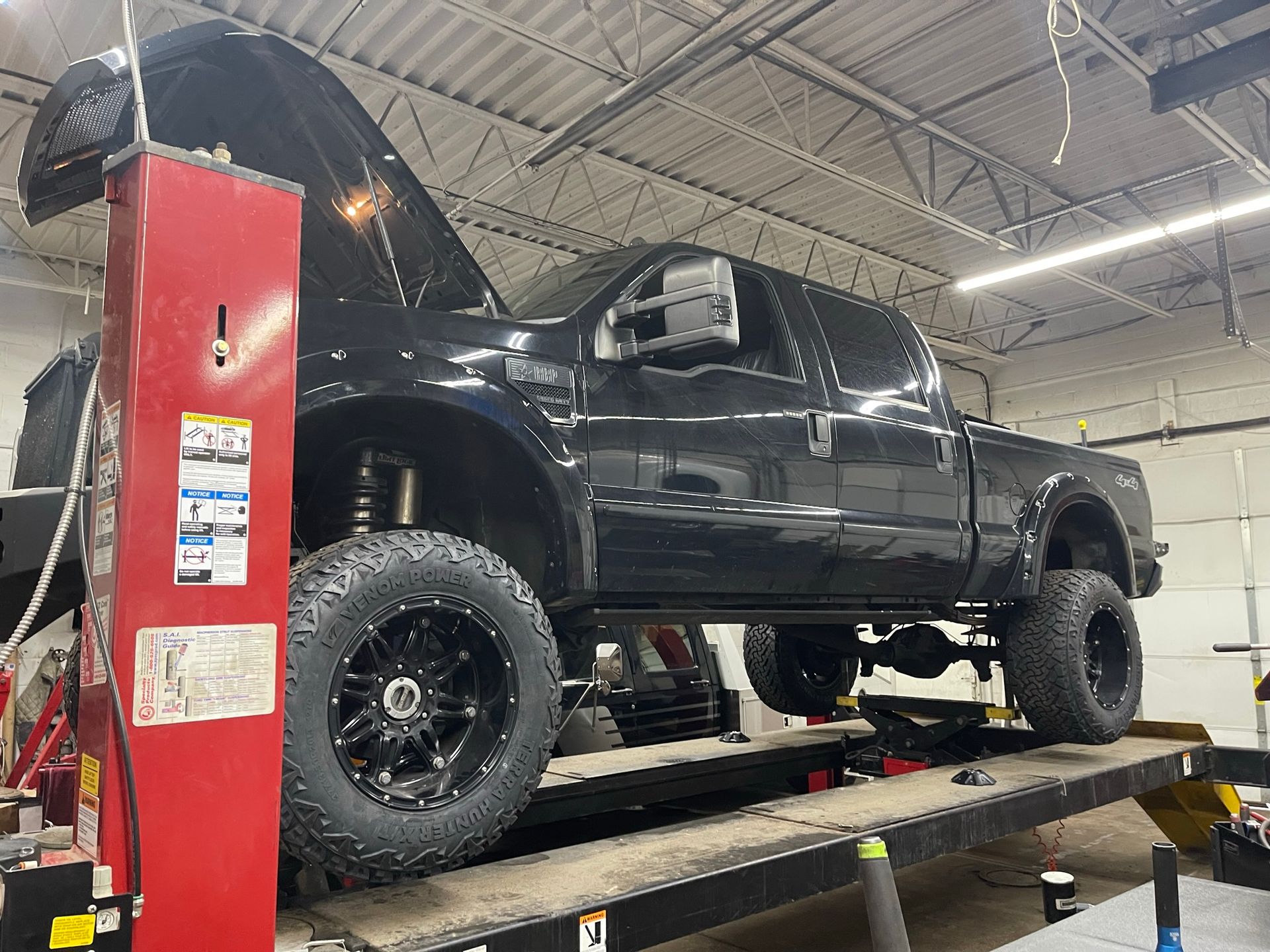 A lifted black truck is sitting on top of a lift in a garage.