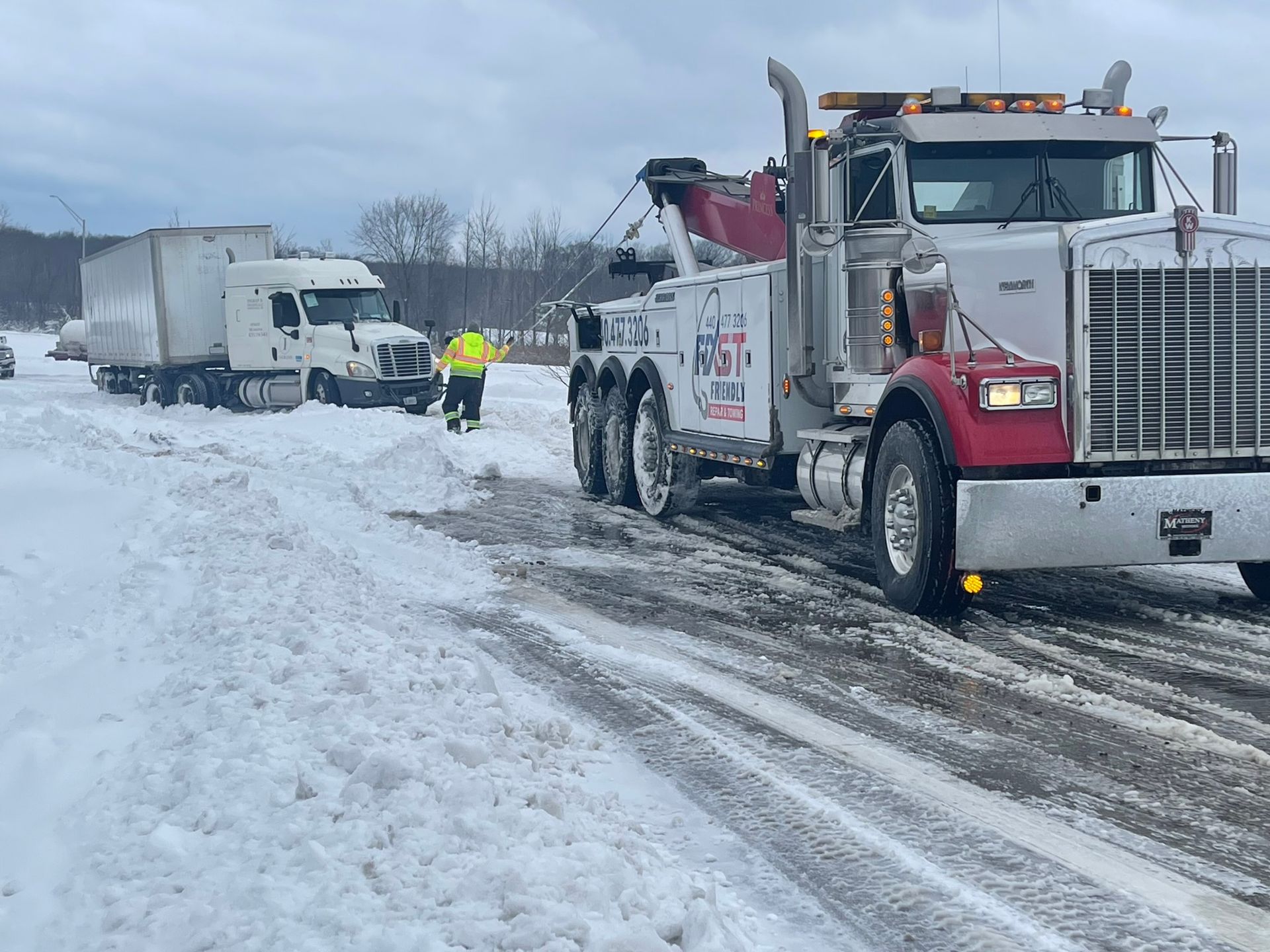 A tow truck is recovering a semi on a snowy road.