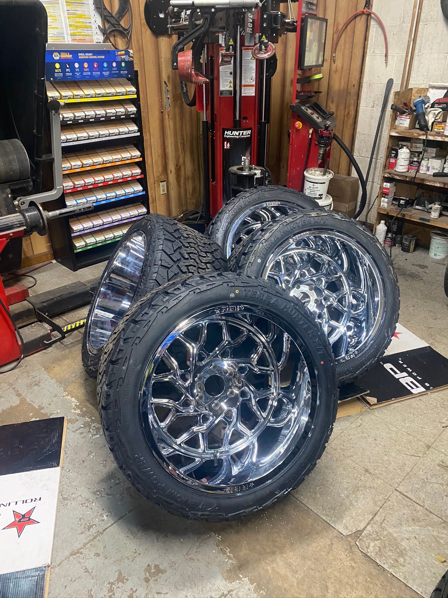 A bunch of tires and wheels are stacked on top of each other in a garage.