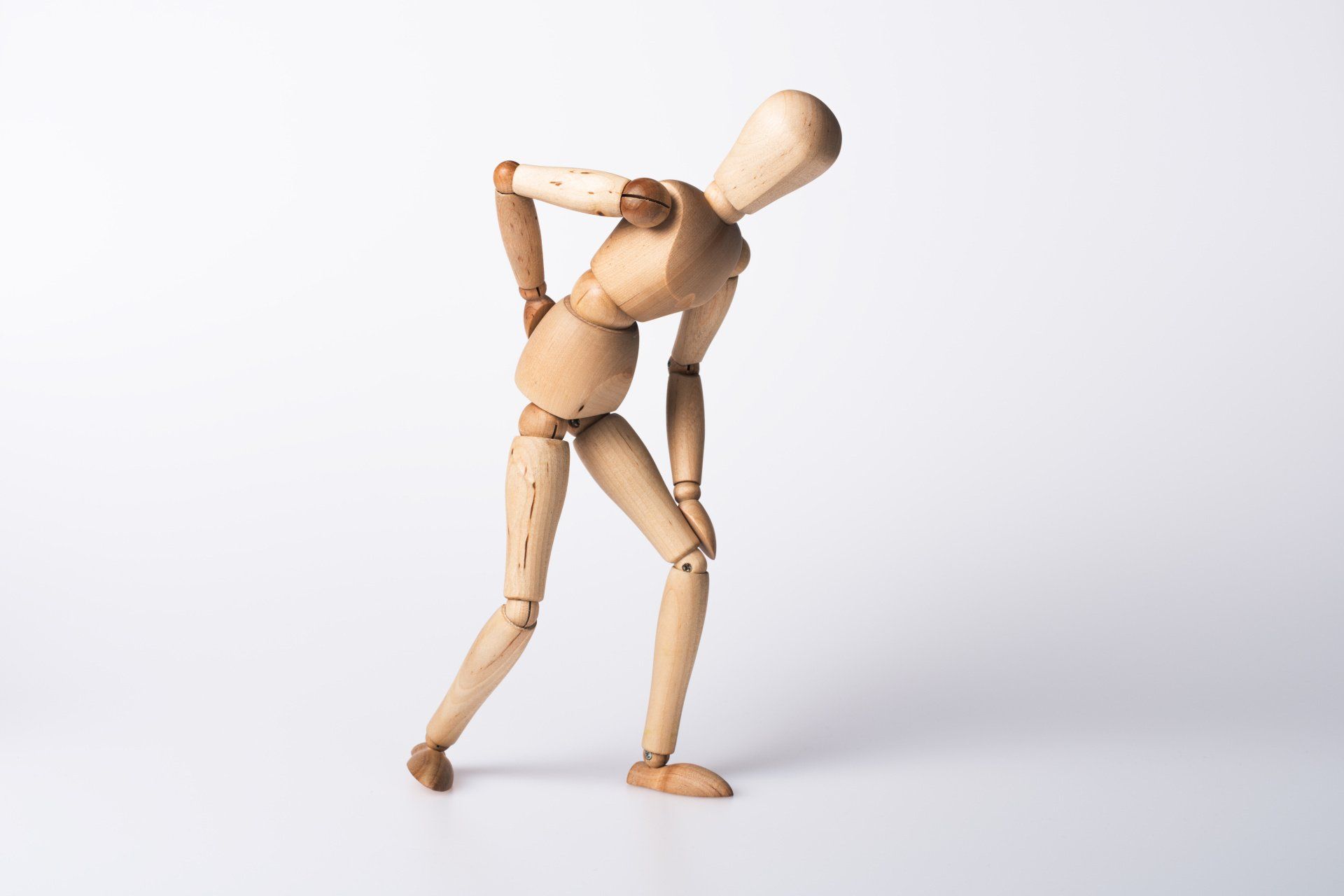 A wooden mannequin is holding his back in pain.
