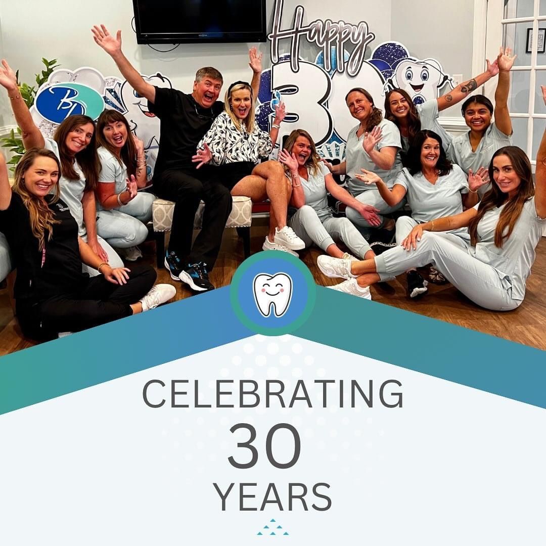 Dental office staff celebrating 30 years. People are smiling, laughing, in a decorated room.