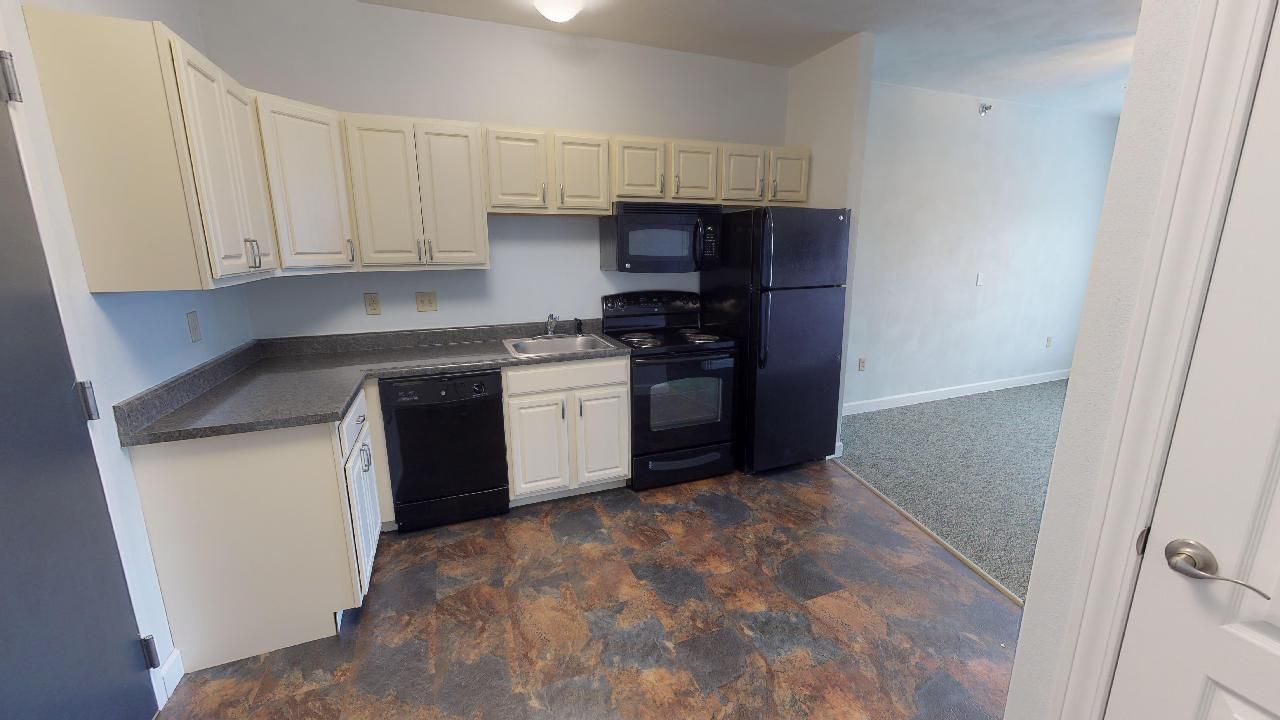 A kitchen with white cabinets , black appliances , and a black refrigerator.