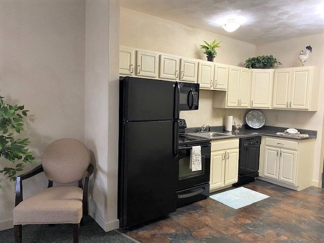 A kitchen with a black refrigerator , stove , microwave , sink and chair.