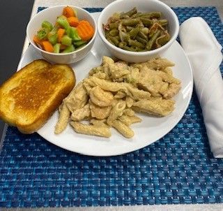 A plate of food with chicken , pasta , green beans , carrots and toast on a table.