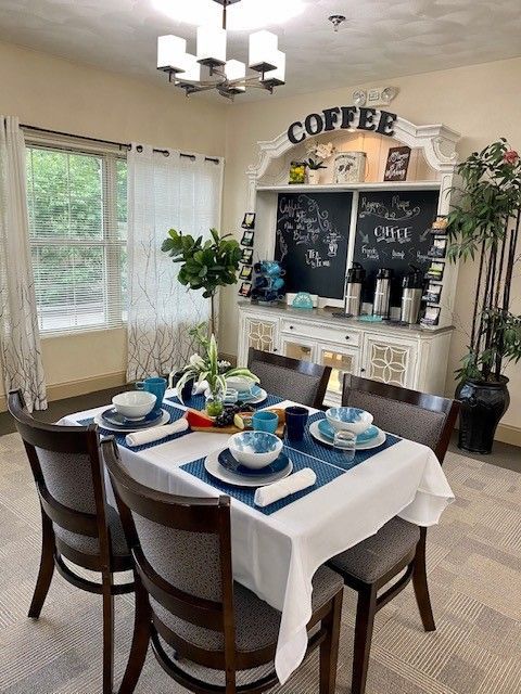 A dining room with a table and chairs and a coffee bar in the background.