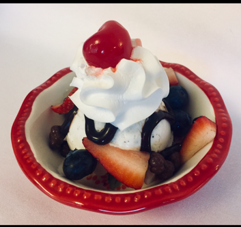 A bowl of ice cream with whipped cream strawberries and blueberries