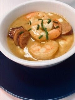 A bowl of soup with shrimp and sausage on a blue plate