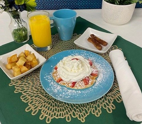 A pancake with whipped cream and strawberries on a blue plate