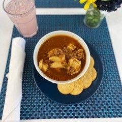 A bowl of soup and crackers on a blue plate on a table.