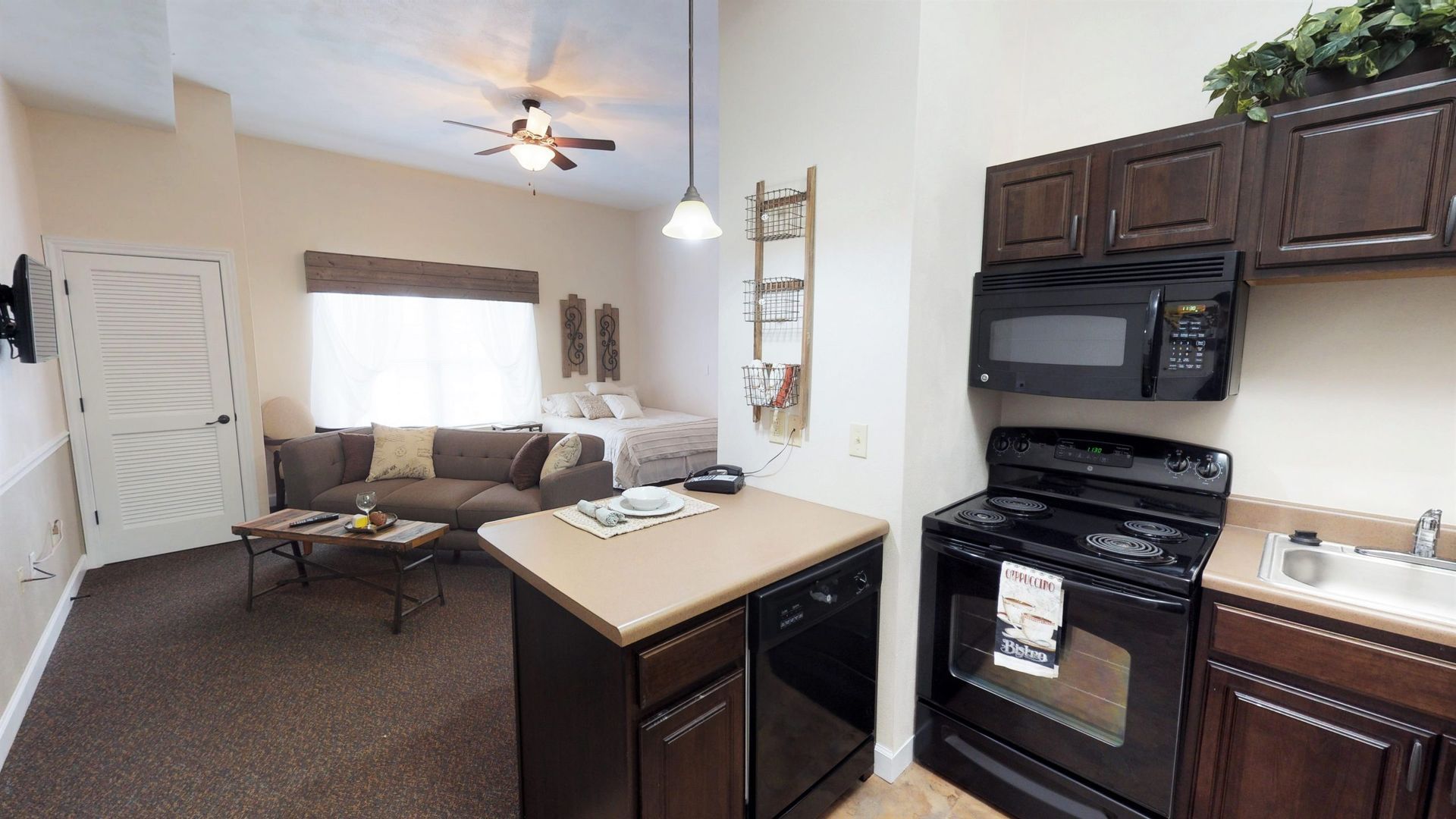 A kitchen with a stove , microwave , sink and a couch.