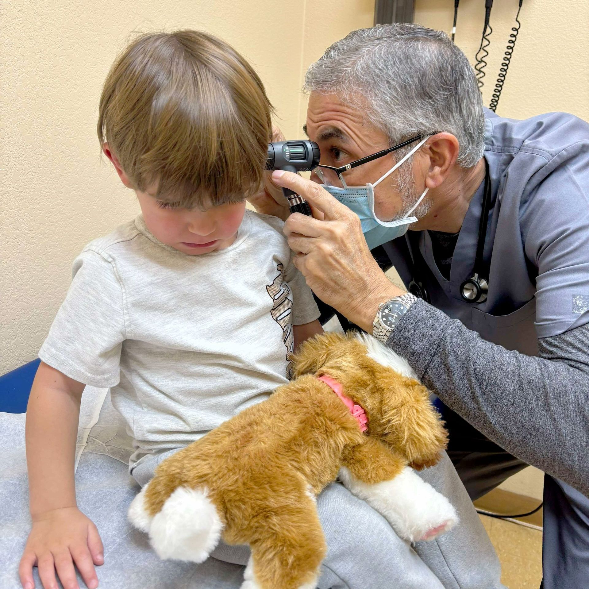 A doctor is examining a young boy 's ear with a stuffed animal.